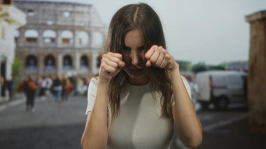 Beyaz tişörtlü genç İspanyol kadın gündüz vakti kolezyumun yanında sokakta yumruklarını sıkıyor; hayal kırıklığı.