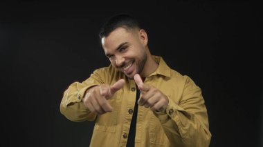 Sarı tişörtlü, geniş ve enerjik bir şekilde gülümseyen İspanyol genç stüdyoyu işaret ediyor..