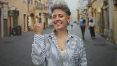 Mağazalar ve bulanık yayalarla dolu işlek bir caddede gülümseyen ve başparmağıyla işaret eden beyaz kadın..