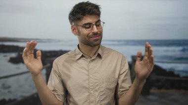 Bej gömlekli adam kollarını açar ve sahilde dalgalarla dalgalanan çıplak avuçlarını gösterir..