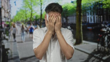 Genç İspanyol adam güneşli şehir caddesinde elleri ile yüzünü kapatır ve jestler reddedilir; hayal kırıklığı.