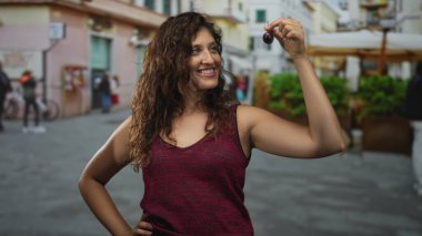 Sokak pazarında parmaklarının arasında kiraz tutan bir kadın. Kolunu kaldırmış ve omzunu açmış. Kendine güveniyor..