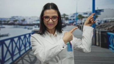 Üniformalı İspanyol kadın bilim adamı bulutlu gökyüzünün altında deniz kenarında gezinirken şaşırmış ve işaret etmiş..