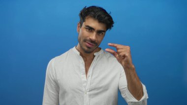 Beyaz gömlekli adam parmaklarını birbirine yaklaştırıyor ve mavi stüdyo ortamında geniş bir gülümseme sergiliyor..