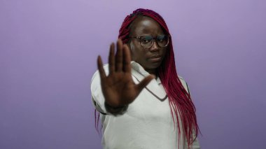 Örgülü ve gözlüklü kadın mor duvara karşı poz veriyor. Beyaz gömlek giymeyi kesiyor. Ayrı bir ortamda kendinden emin bir şekilde kınama ve yetkilendirme gösteriyor..