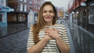 Arkadaki bulanık dükkanlarla ıslak şehir caddesinde duran sandık üzerinde el ele tutuşan genç beyaz kadın, minnettarlık..