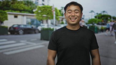 Siyah tişörtlü adam gülümsüyor ve şehir sokağında dikilirken dilini dışarı çıkarıyor. Bulanık arabalarla dolu. Neşeli neşe.