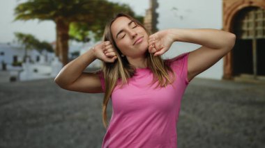 Pembe tişörtlü bir kadın, sabah enerjisini ve rahatlığını ifade ederek, canlı bir şehir zemininde, canlandırıcı bir pozitiflik ve gençlik ruhu içinde bir sokağa uzanıyor..