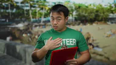 Plaj geçmişinde panosu olan gönüllü gömlekli bir adam, açık hava, deniz kenarı, yardım, toplum ve birlik temaları üzerine odaklanıyor, hayır veya sosyal nedenler için ideal.