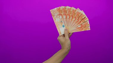Beyaz adamın elinde Filipinli peso banknotları, parlak mor bir arka plan, sergilenen finansal kavramlar ve para birimi odaklı.