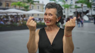 Gri saçlı yaşlı kadın hareketli bir şehir caddesinde para kazanırken gülümsüyor, açık şehir arka planına karşı hareketli ve hayat dolu..