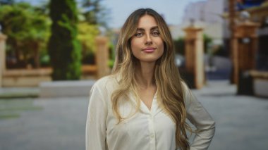 Omuzlarının üzerinden uzun saçlı genç sarışın kadın yukarı bakıyor güneş ışığında taş avluda; merak yansıması.