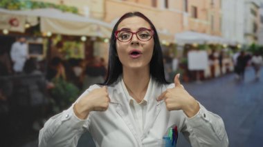 Laboratuvar önlüklü kadın, arka planda açık hava ortamında genç bilim adamını sergilemek için yoğun bir sokakta enerjik bir şekilde sesleniyor.