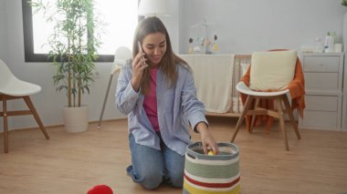 Kadın telefonda konuşurken rahat bir bebek odasında oyuncaklar düzenliyor, ev hayatı tasviri için doğal ışık ve yumuşak dekorlarla modern bir iç mekan sergiliyor..