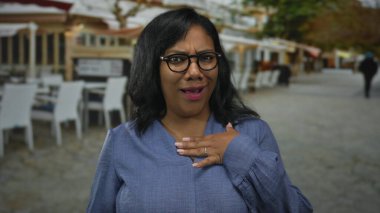 Afro-Amerikalı bir kadın konuşuyor ve elleri göğsünde olan mavi bir bluz giyiyor..