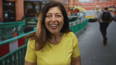 Sarı tişörtlü kadın ağzı açık gülümsüyor ve inşaat bariyerinin yakınındaki caddeyi işaret ediyor. Mutluluk..