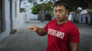 Can kurtaran tişörtlü ve boynunda ıslık olan bir adam sokak duvarını işaret ediyor..