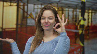 Mavi kazaklı genç beyaz kadın inşaat alanının önünde el işareti yapıyor, onaylandı..