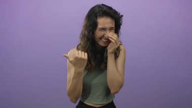 Yeşil mahsullü kadın elleriyle ağzını kapatırken gülüyor ve stüdyoda başparmağını işaret ediyor..