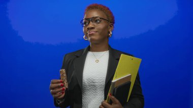 Gözlüklü genç kadın stüdyoda yan yana bakarken granola çubuğu ve sarı pano tutuyor; tefekkür.