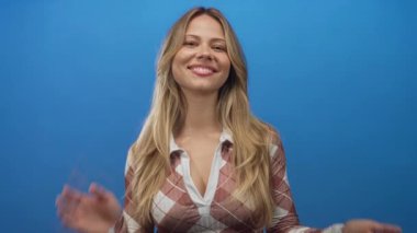 Kadın stüdyoda uzun sarı saçlı ve gülümseyen yüzüyle el çırpıyor; kutlama onayı eğlenceyi teşvik ediyor.