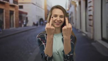 Şehrin arka planında ifade vermek için orta parmakları mizahi bir şekilde kaldırılmış, günlük ekose gömlekli bir kadın..
