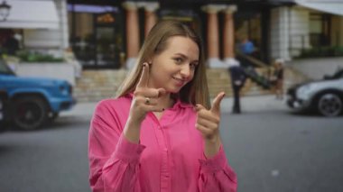 Kadın gülümsüyor ve kentin pozitif enerjisini gösteren parlak pembe bir tişört giymiş bir şekilde kentin caddesini işaret ediyor..