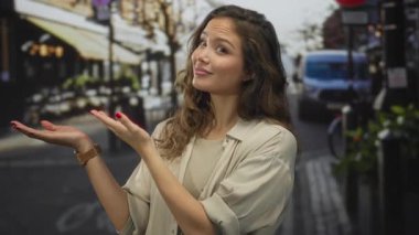 Latin kökenli genç bir kadın, bir sokak terasında iki elini de uzatıyor; sıcak bir davet..