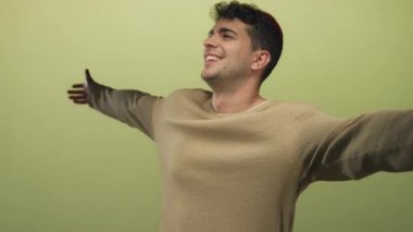Man stretches arms in studio setting by young hispanic male smiling open against green backdrop.