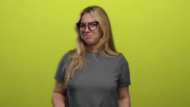 İğrendiğini ifade eden bir kadın, yeşil arka plan önünde ellerini kaldırmış, gözlük takmış, açıkça onaylamayan ve olumsuz duygular besleyen bir kadın.