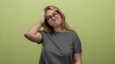 Yeşil arka plana karşı hayal kırıklığı gösteren el ele hareket eden gözlüklü ve günlük gri gömlekli bir kadın..