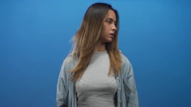 Uzun saçlı, gri tişörtlü bir kadın mavi stüdyoya bakıyor. Bakışları çevrilmiş üç çeyrek portre; tefekkür.