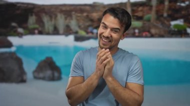 Güneşli bir tatil köyünde havuz kenarında gülümseyen genç İspanyol adam coşkulu bir otel atmosferinde neşeli bir yaz havası yaratıyor..
