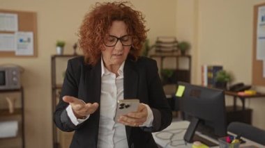Modern ofis ortamında akıllı telefon üzerinde çalışan bir kadın, profesyonel bir çevrede odaklanma ve konsantrasyon sergiliyor..
