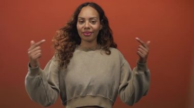 Kadın stüdyoda her iki işaret parmağı ile göğsü işaret eder turuncu arka plan ile; özgüven kendini güçlendirme.