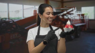 Önlüklü kadın elinde tatlı kasesi tutarken ve parmaklarıyla bovling oynarken endüstriyel yapı içinde gülümserken; keyif konukseverliği.