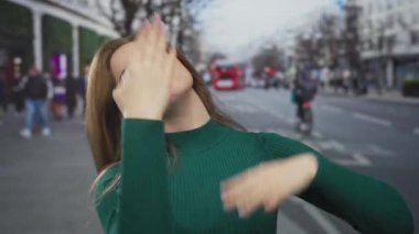 Başı öne eğilmiş bir kadın, binalarla dolu, hareketli bir caddede diş ağrısı için yanağını geriye doğru uzatıyor..