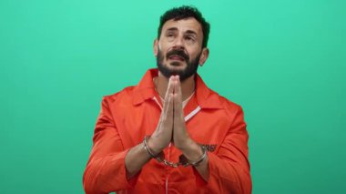 Turuncu tulumlu, sakallı ve kelepçeli, yeşil arka planda duran İspanyol adam duygusal bir ifade sergiliyor..