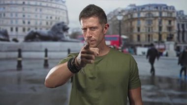 Adam, aslan heykeli ve tarihi bina yakınlarındaki işlek bir şehir meydanında ıslak bir caddeyi işaret ederek kameraya doğru uzanan eli işaret ediyor; suçlama.