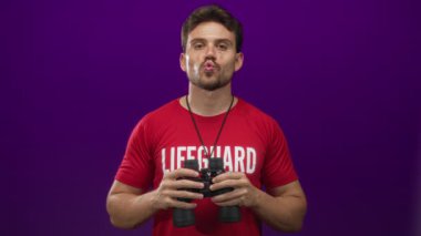 Kırmızı tişörtlü bir adam elinde dürbün ve dudak bükerek mor stüdyo arkaplanına karşı oynuyor..