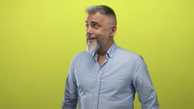 Orta yaşlı, mavi gömlekli bir adam yeşil bir stüdyoda el hareketleriyle işaret ediyor; şaşkın, neşeli bir enerji..