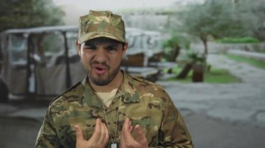 Yeşil kamuflaj üniforması giyen, bulanık ağaçlı adam yüzünü ekşitiyor; tiksinti.