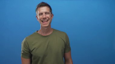 Stüdyoda el sıkışmak için elini uzatan, gözlüklü ve zeytin yeşili tişörtlü adam; dostça selamlaşma.