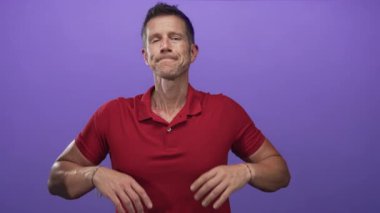 Avuç içleri havada omuz silken ve mor stüdyoda kırmızı polo tişört giyen bir adam; belirsizlik kararı.