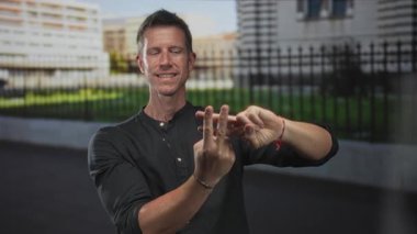 Adam parmaklarıyla hashtag yapıyor, gülümsüyor ve demir çitli, açık havada binanın önünde çıplak ellerini gösteriyor; eğlenceli sosyal medya.