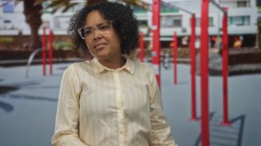 Kadın, palmiye ağaçları ve sağlam kırmızı yapılar ile sokak spor salonu parmaklıklarında ellerini uzatıyor; kararlılık.