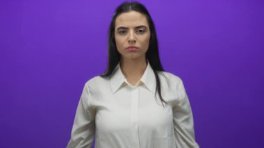 Beyaz gömlekli bir kadın, parlak mor bir duvarın önünde kolları çapraz duruyor, ciddi bir ifadeyi yansıtıyor, minimalist bir ortamda kararlılık ve güven öneriyor..