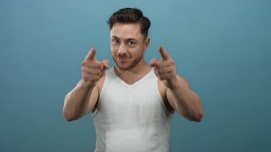 Beyaz kolsuz tişörtlü genç adam mavi arka planda kameraya doğru hareketler yapıyor, dostluğu ve davetiyeyi ifade ediyor..