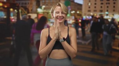 Kadın, siyah spor sutyen ve gri tayt giyerek avuç içlerini kaldırıyor. Meşgul şehir caddesinde çıplak göbeğiyle gülümsüyor. Geceleri yayalarla dolu..