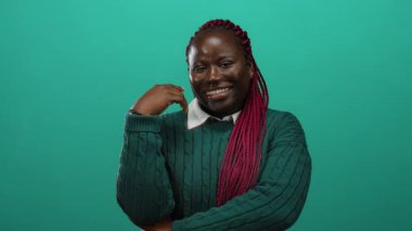 İzole edilmiş yeşil arka plana gülümseyen yeşil süveter giyen neşeli bir ifadeyle canlı pembe örgüler takan mutlu ve kendine güvenen bir kadın..